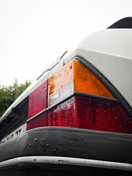 Close-up of a classic white car's rear taillight, featuring raindrops for a vintage feel.