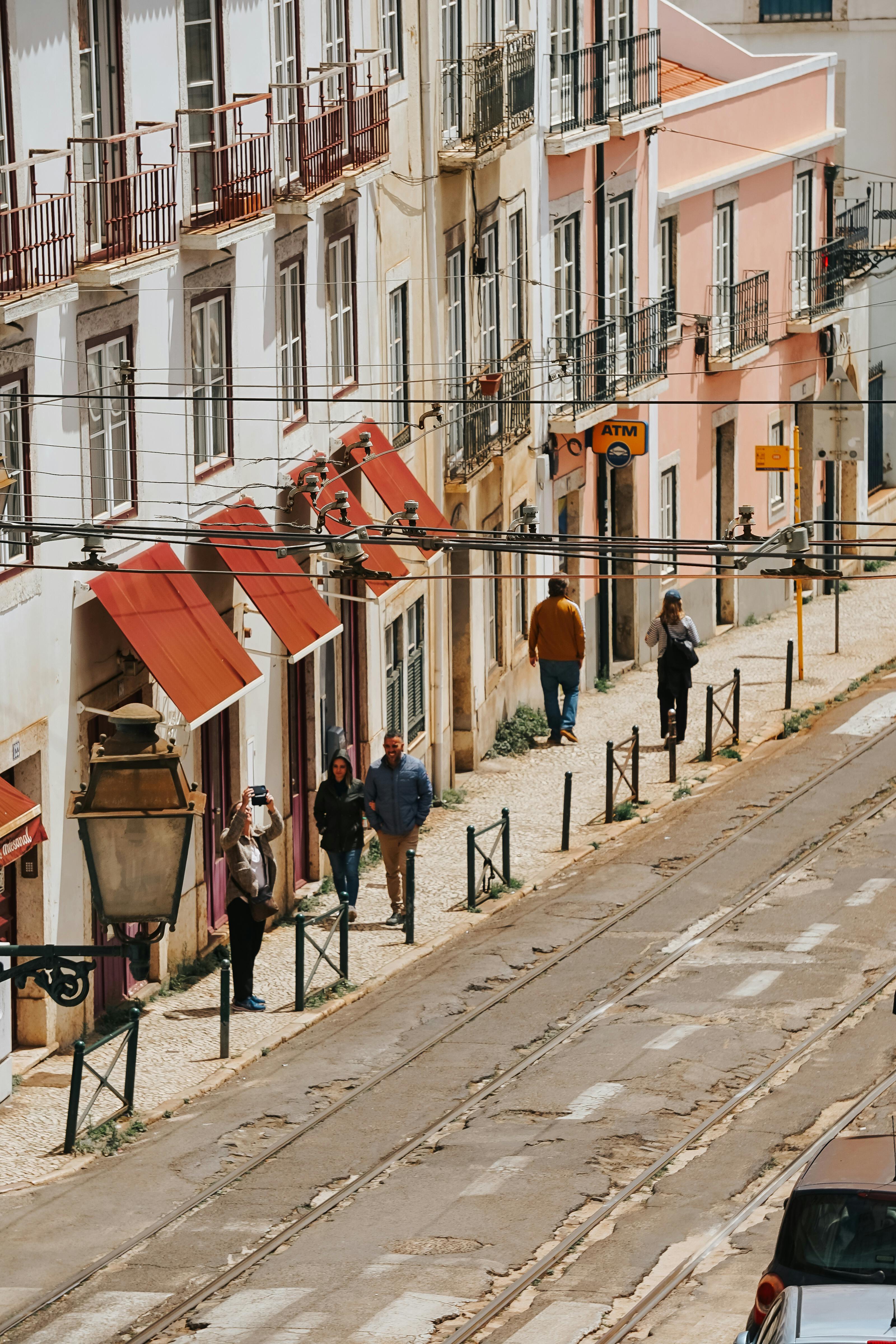 A picturesque European street with pedestrians walking alongside colorful buildings under a cloudy sky.