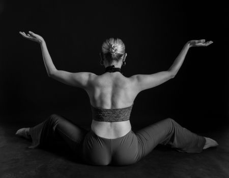 A woman performs a graceful dance pose with extended arms in a black and white studio setting.