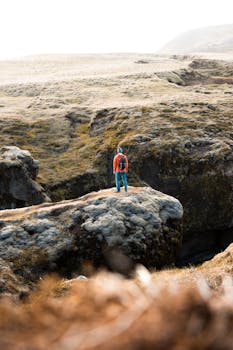A lone hiker stands on rocky terrain in Vik í Mýrdal, Iceland, showcasing breathtaking outdoor scenery.