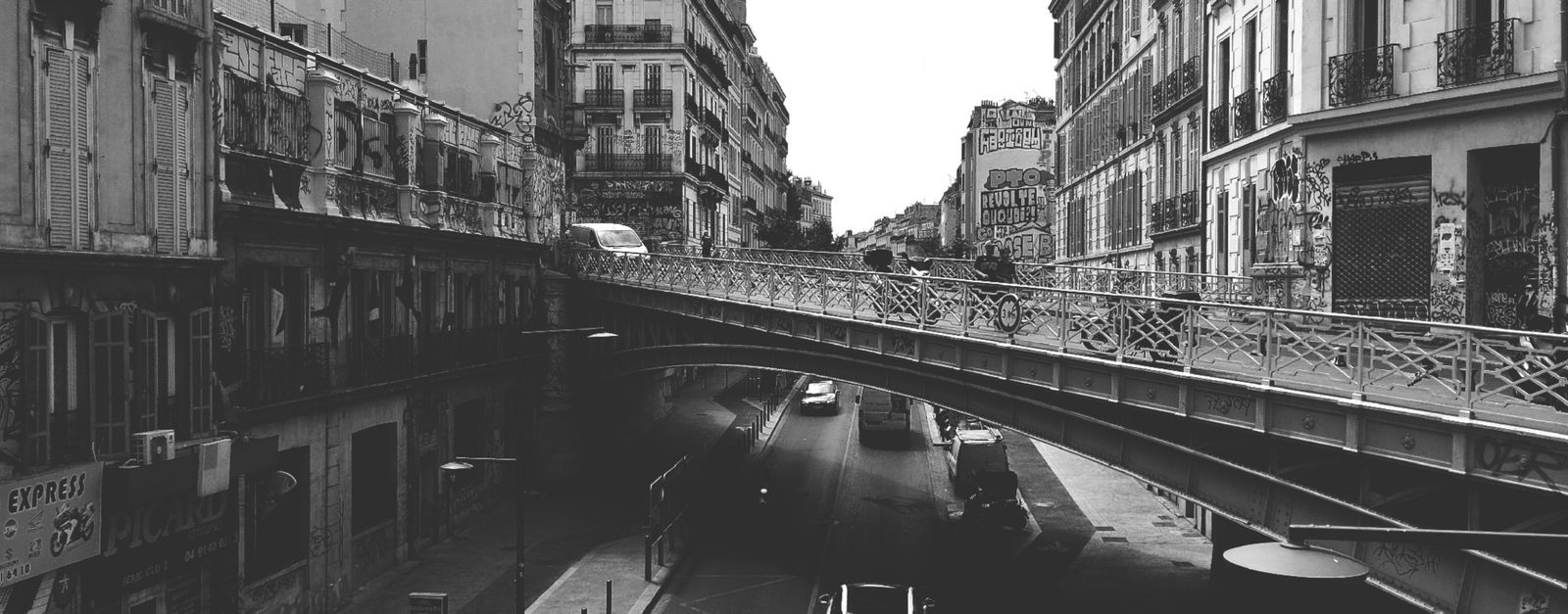 Monochrome urban scene featuring a bridge over a busy street, captured in a historic city.