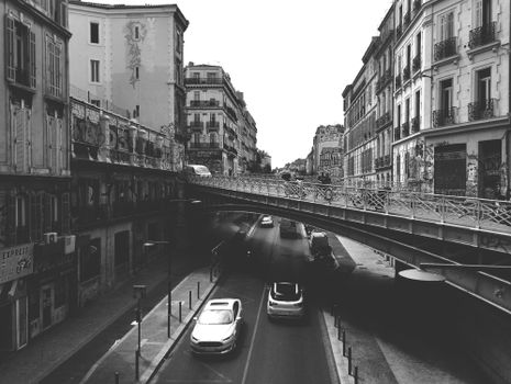 Monochrome urban scene featuring a bridge over a busy street, captured in a historic city.