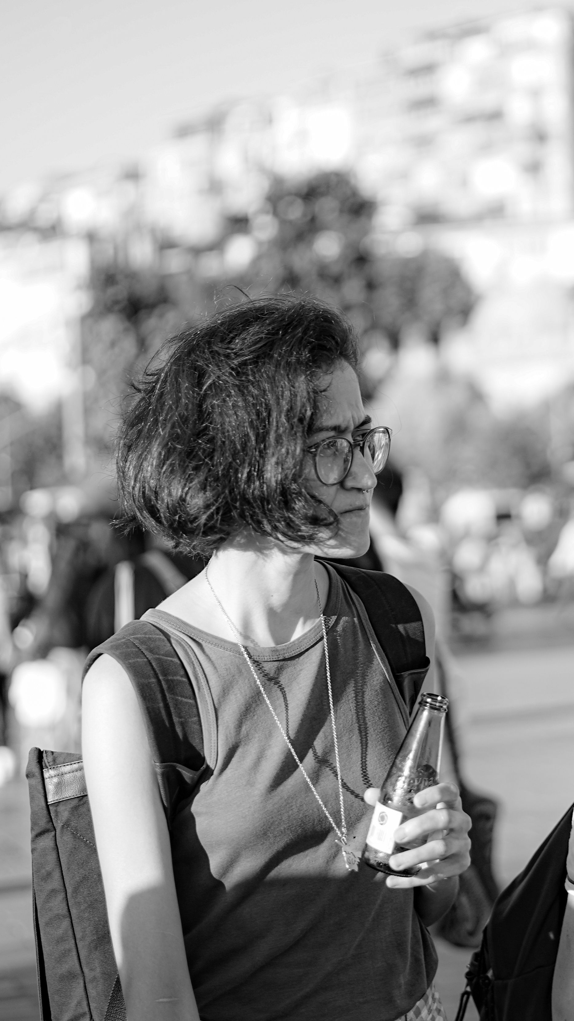 Black and white candid portrait of woman holding a bottle outdoors.