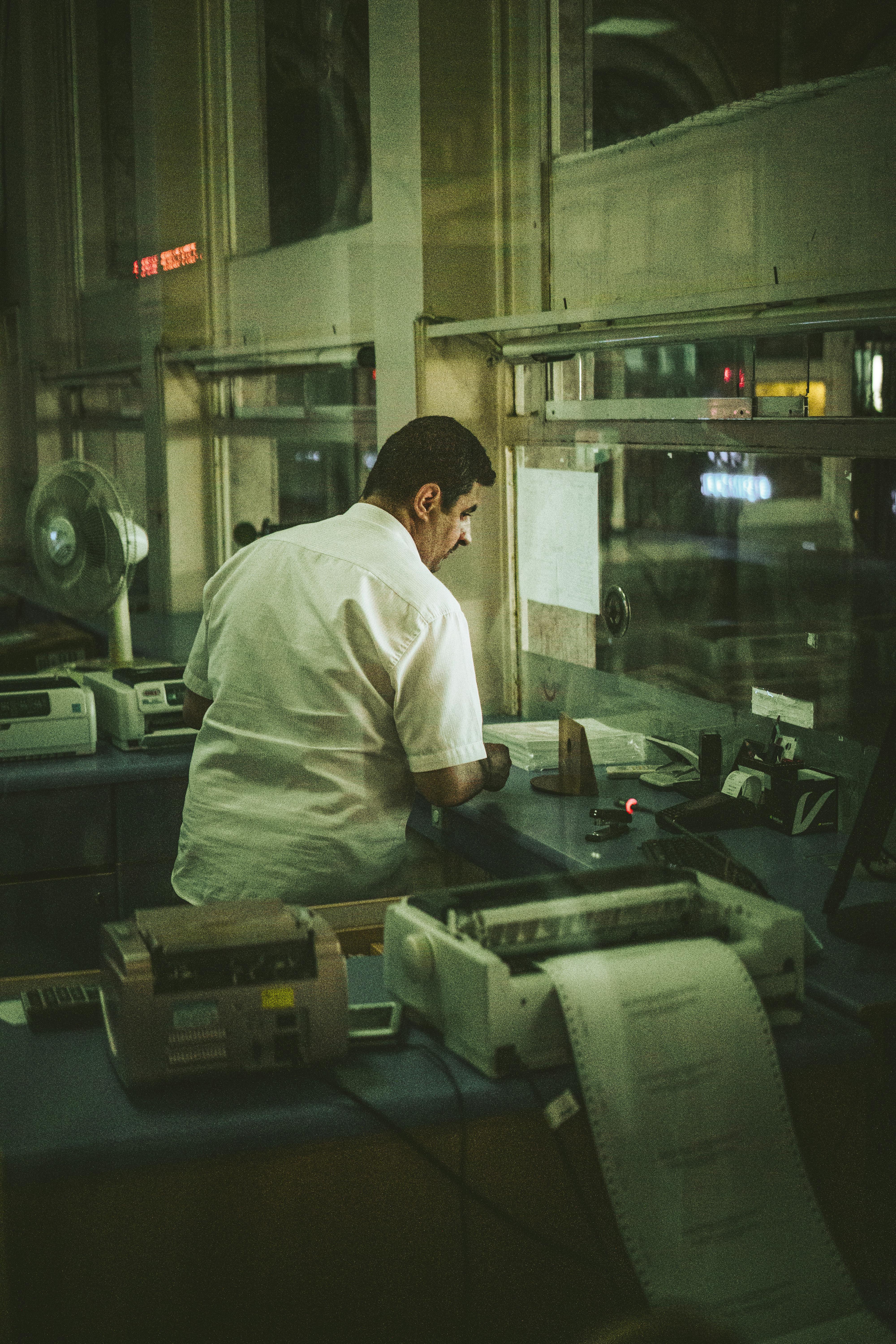Office worker handling paperwork with vintage machines at night in an illuminated workspace.
