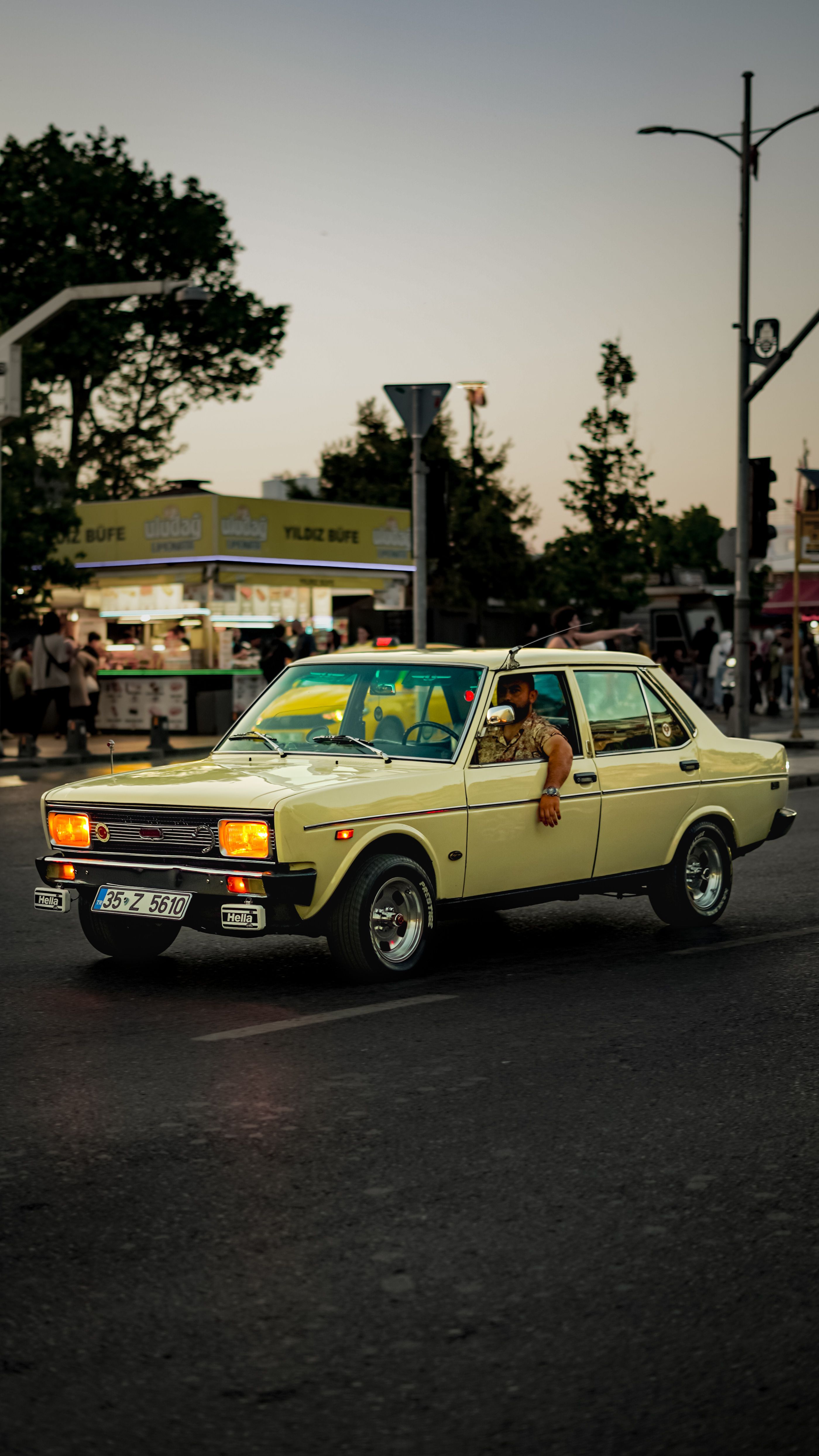 Fotomural Un coche retro circulando por las calles de la ciudad durante el atardecer, capturando la esencia urbana.