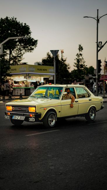 Fotomural Un coche retro circulando por las calles de la ciudad durante el atardecer, capturando la esencia urbana.