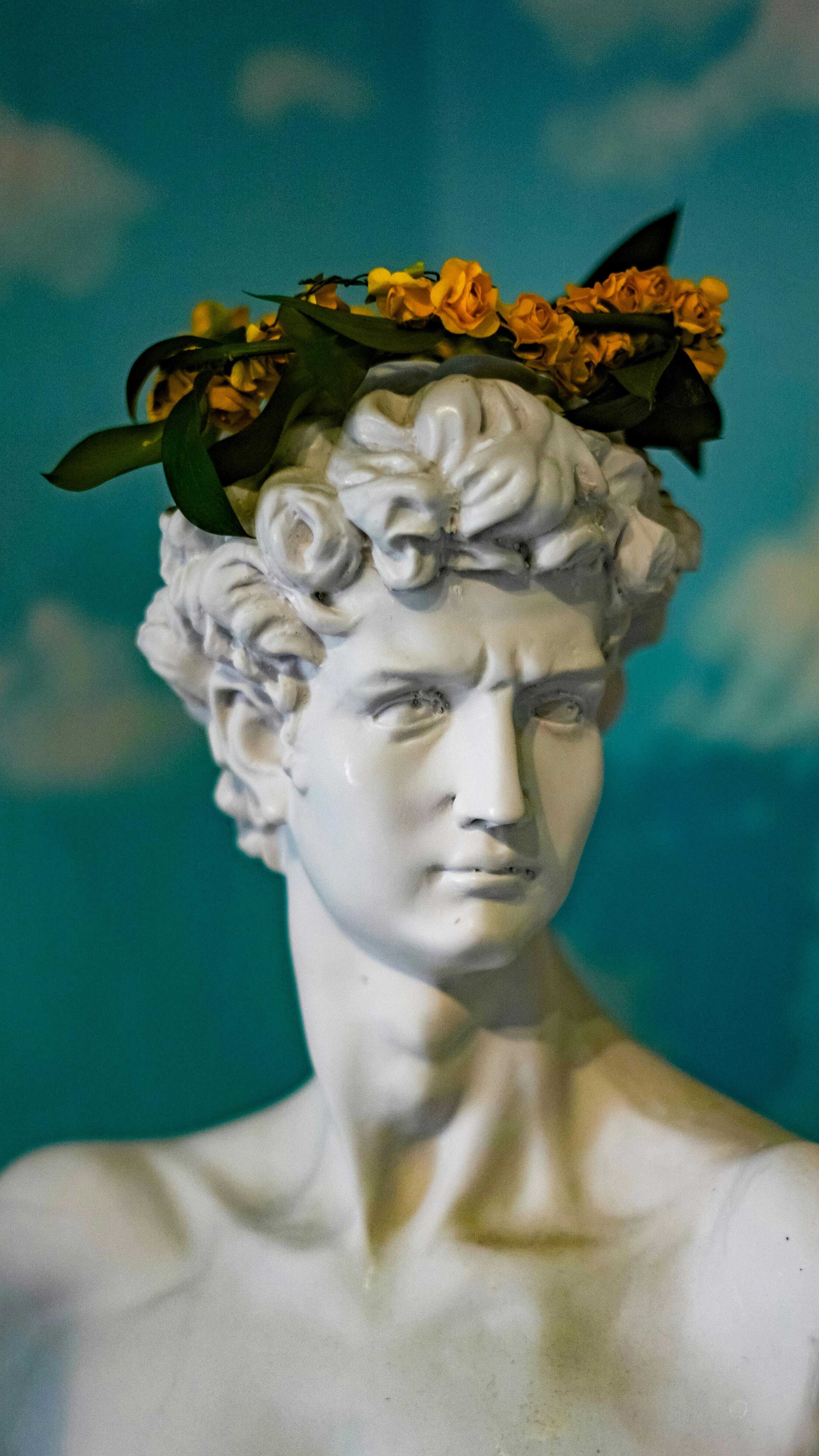 A classic marble bust adorned with a floral crown, set against a sky backdrop.