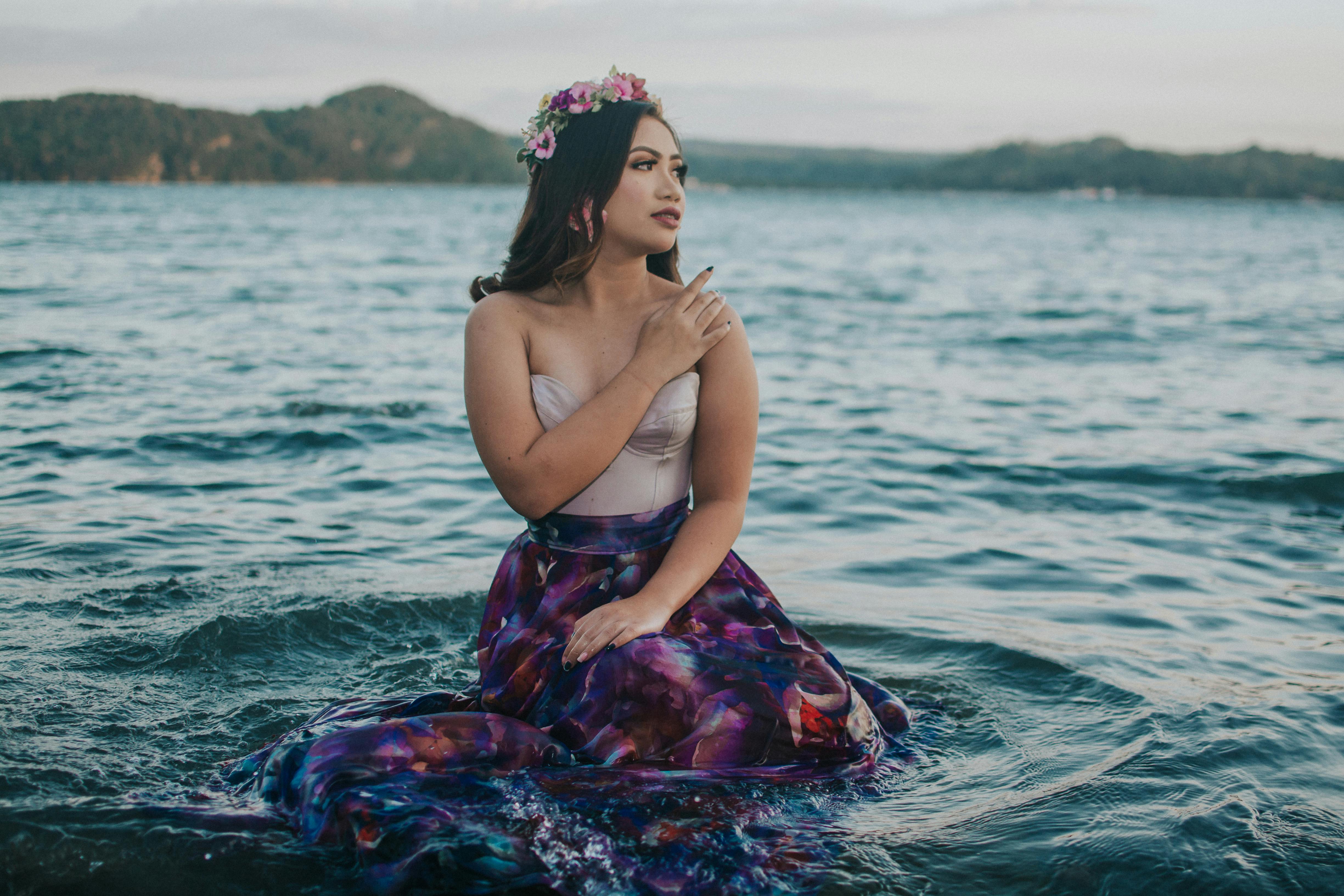 一位头戴花卉王冠、身着彩色连衣裙的女子，优雅地坐在大海中，尽显宁静与优雅