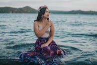 一位身着彩色连衣裙、头戴花卉王冠的女子优雅地坐在大海中，体现着优雅与宁静