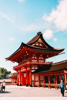 Colorful view of the historic Fushimi Inari Taisha Shrine with visitors under a blue sky in Kyoto, Japan.