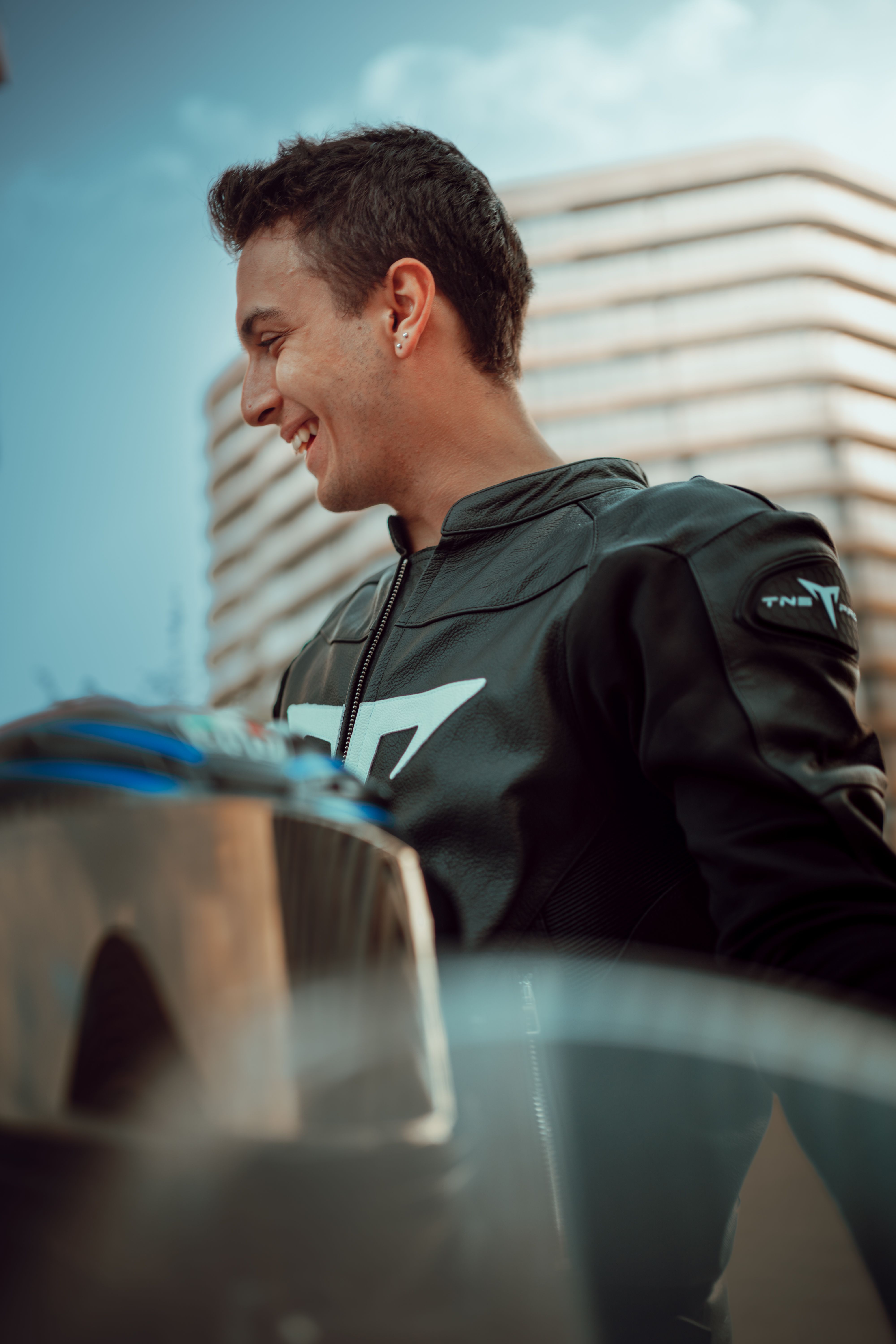 Portrait of a smiling motorcyclist in a leather jacket in İstanbul's urban backdrop.