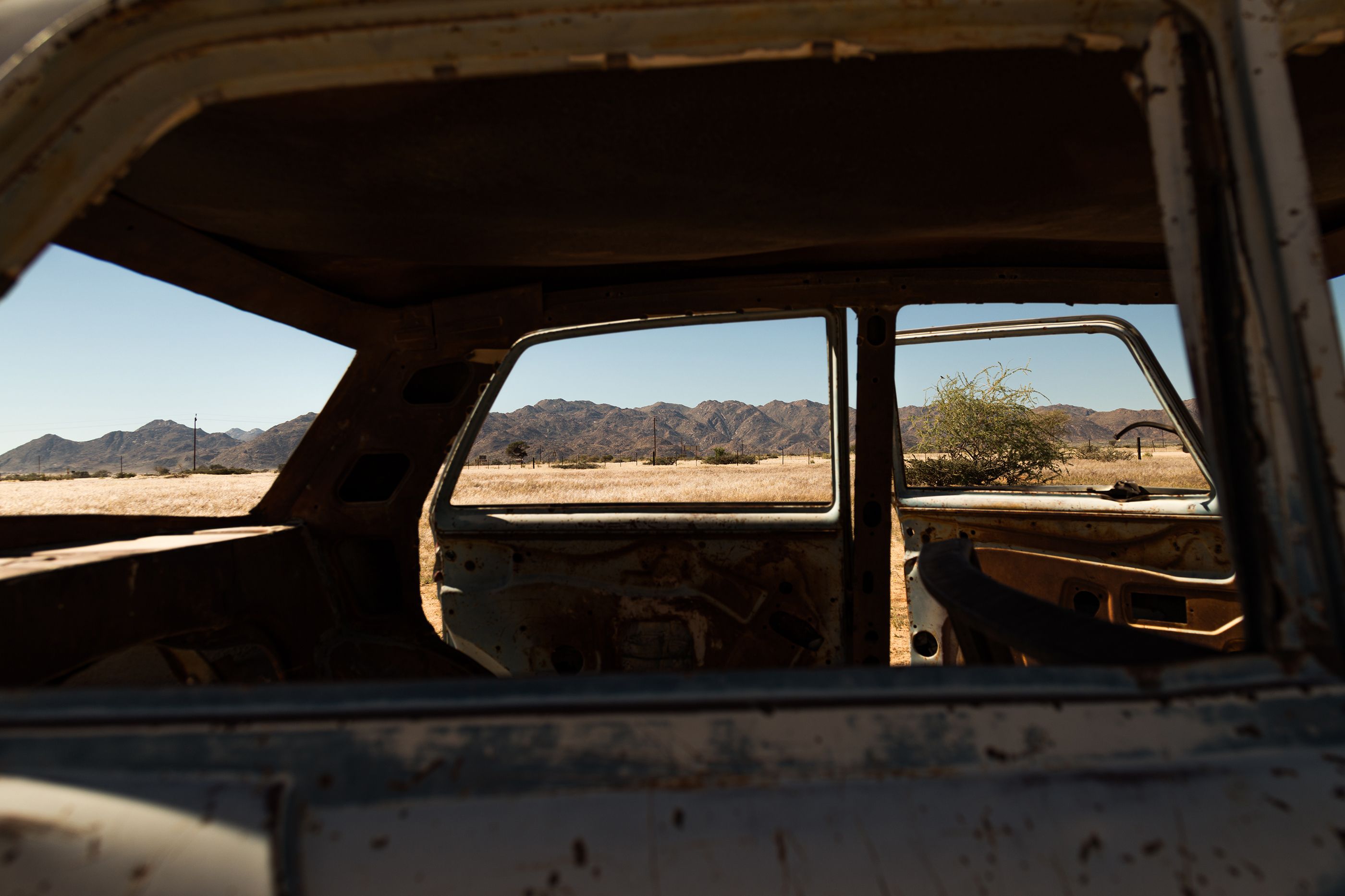 Rusty, abandoned car interior with scenic desert view, framed against distant mountains.
