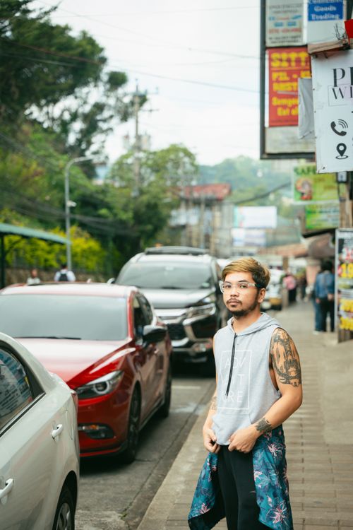 Free Stylish man in tank top with tattoos stands on lively city street, showcasing urban fashion. Stock Photo