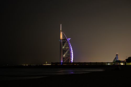 Free Modern sail shaped building with neon lights located on shore of calm sea against cloudless night sky in Dubai Stock Photo