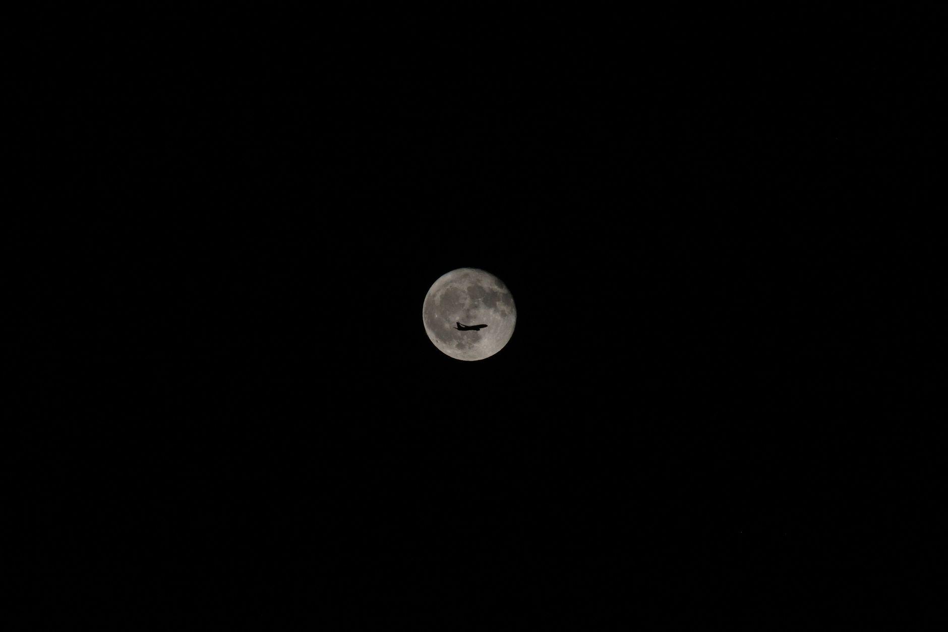 An airplane silhouette against a bright full moon in a clear night sky, showcasing travel and exploration.