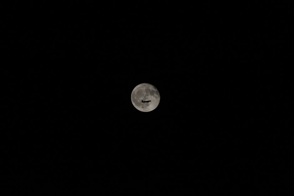 Fotomural Una silueta de avión contra una brillante luna llena en un cielo nocturno claro, mostrando viajes y exploración.