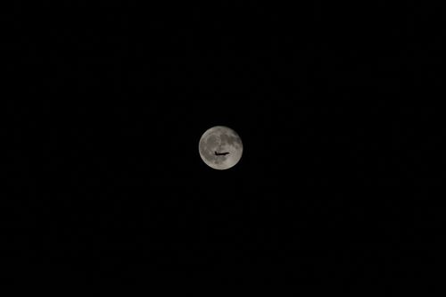 Free An airplane silhouette against a bright full moon in a clear night sky, showcasing travel and exploration. Stock Photo