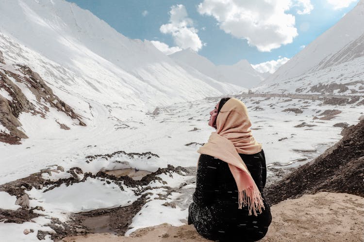 Woman In Black Dress Sitting On Rock At The Valley Covered In Snow