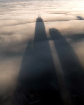 Aerial view of skyscraper shadows casting on dense cloud cover, creating a dramatic silhouette.