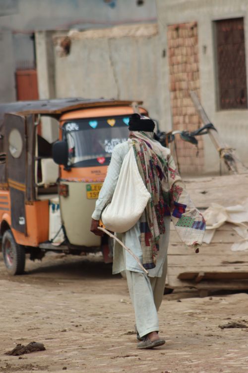 Free A man walks on a rustic city street near a colorful rickshaw, exuding a warm street vibe. Stock Photo