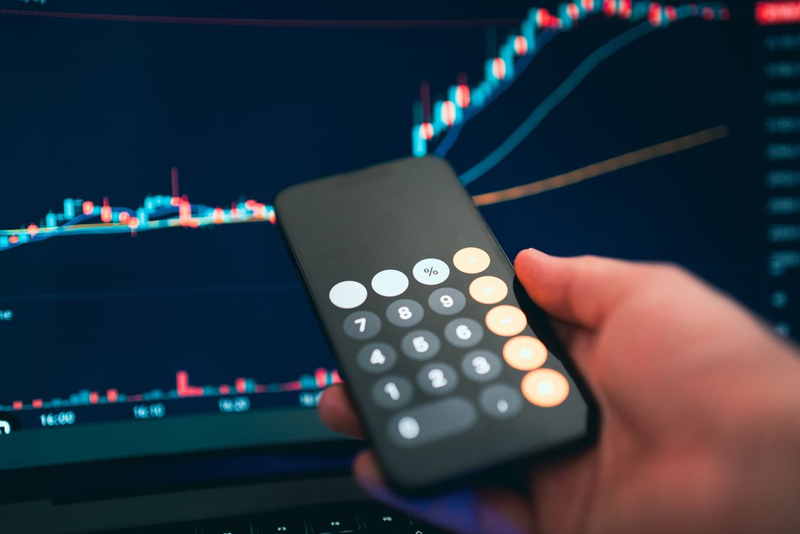 Free Close-up of a smartphone displaying a calculator with a financial chart in the background. Stock Photo