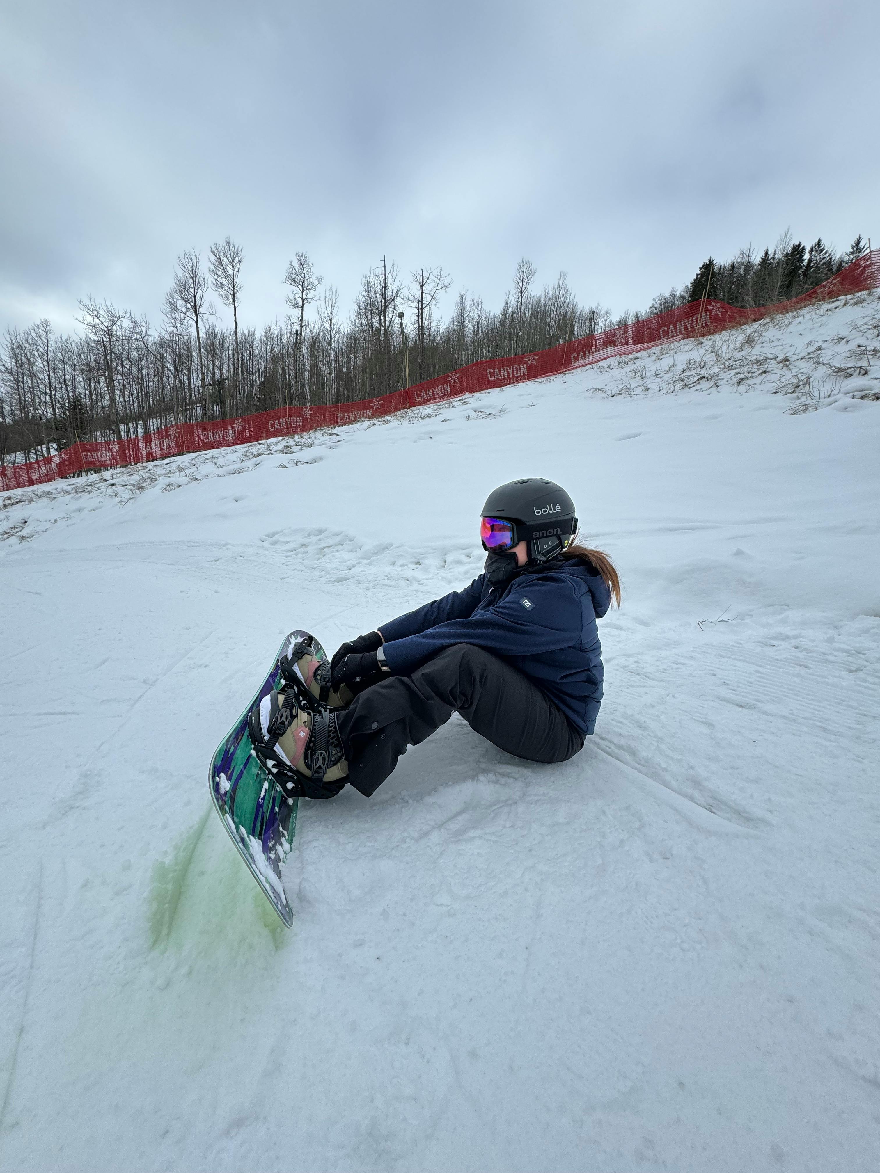 Prescription Goggle Inserts - A woman sits with her snowboard on a snowy mountain slope, ready for action in winter.