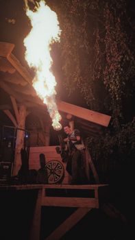 A thrilling night fire performance with a performer on a wooden stage under trees, captured in vibrant light.