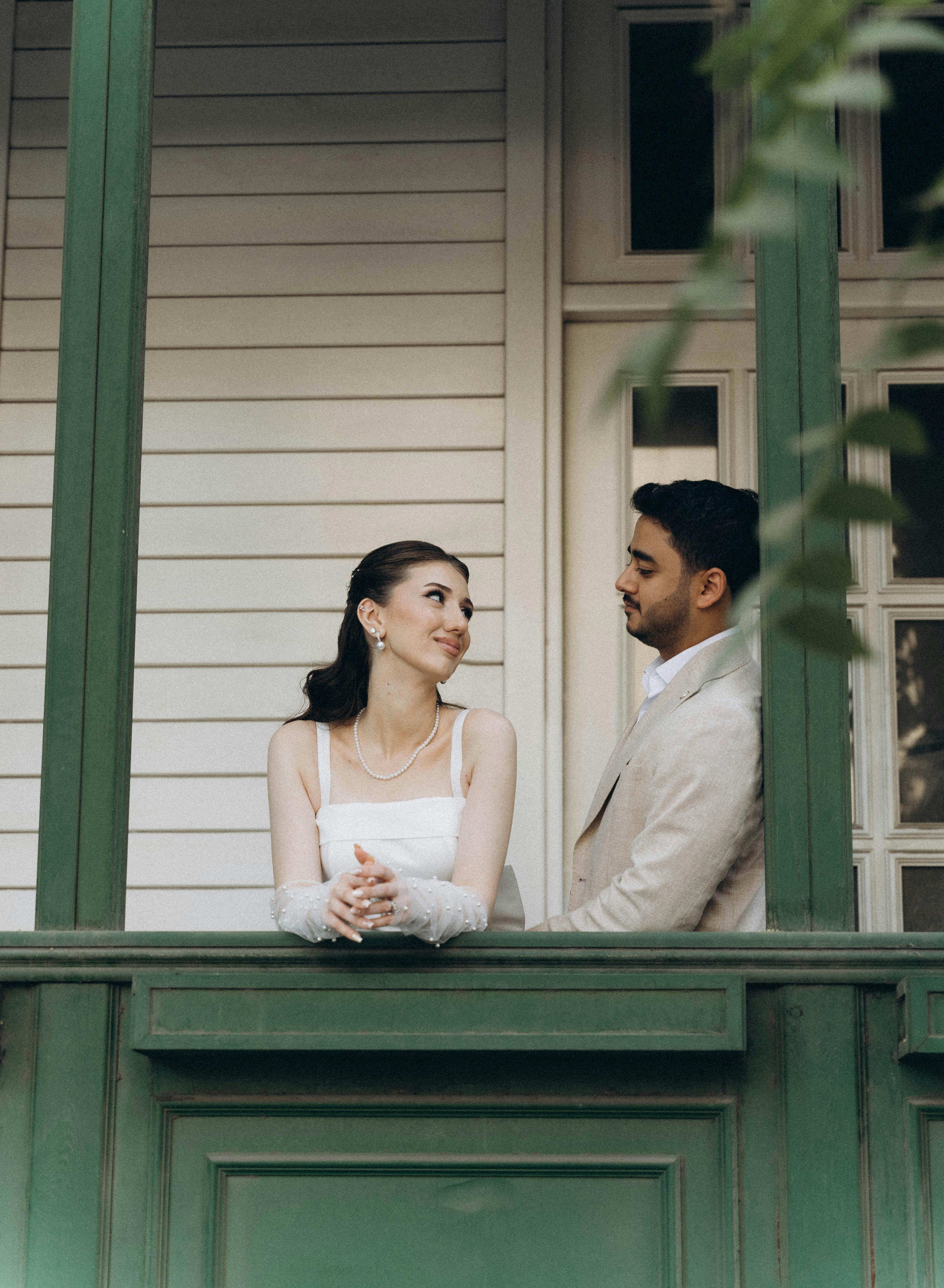 A loving couple enjoys a serene moment on a vintage balcony in their wedding attire.