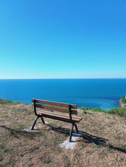 Free Peaceful hilltop bench overlooking the vast ocean under a clear blue sky, perfect for relaxation. Stock Photo