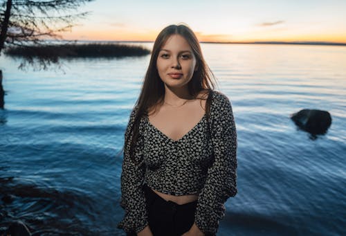 A girl standing in front of the water at sunset