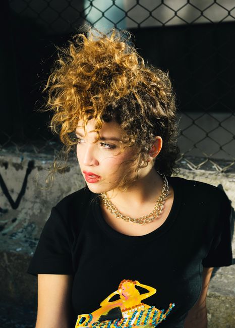 Stylish young woman with curly hair and bold makeup in an urban environment.