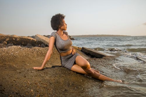 Free Woman in a silver outfit lounging on a rocky beach with waves in the background. Stock Photo