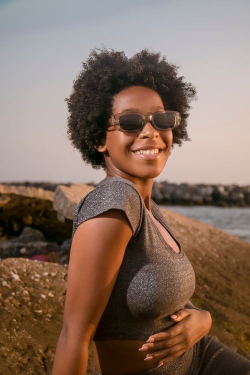 Free A cheerful woman with curly hair enjoys a sunny day at the beach in Luanda, Brazil. Stock Photo