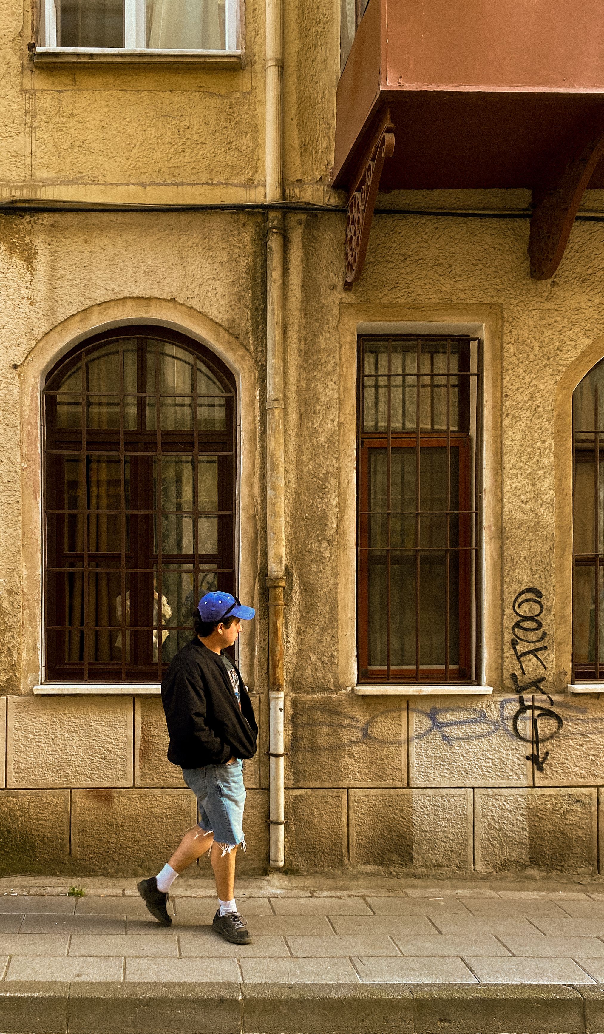 A man walks by an old tenement building adorned with graffiti in a city street
