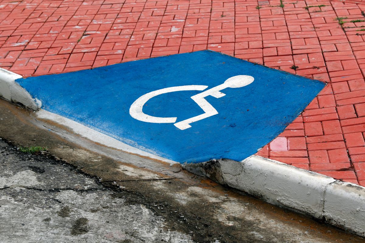Close-up of a blue handicap parking symbol on a red brick pavement. Illustrative editorial photograph.