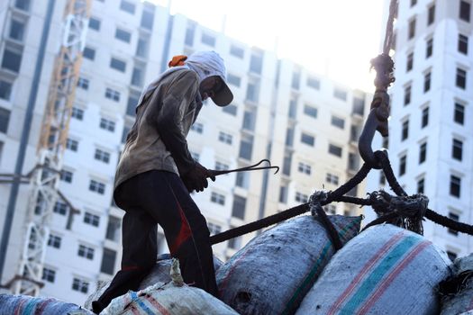 A construction worker manages crane load with sacks at an urban site in Jakarta.