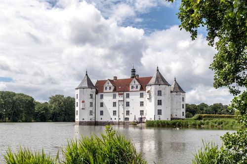 Free Historic Glücksburg Castle in Germany reflecting on a serene lake under a cloudy sky. Stock Photo