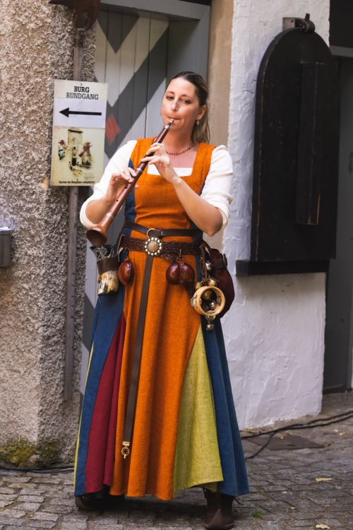 Free A woman in a colorful medieval dress plays a flute on a cobblestone street. Stock Photo