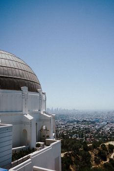 View of Griffith Observatory with Los Angeles skyline in the distance under a clear blue sky.