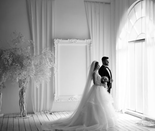 Free Black and white photo of a bride and groom standing by an arched window in an elegant venue. Stock Photo