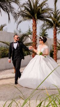 Bride and groom walking hand in hand outdoors amid palm trees, capturing a joyful wedding moment.