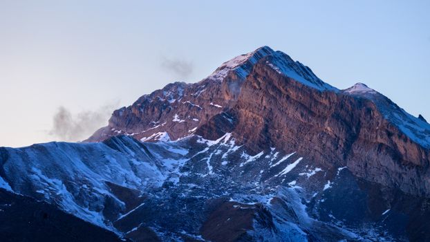 Majestic rocky mountain peak covered in snow with soft sunlight illuminating. Perfect for winter landscapes.