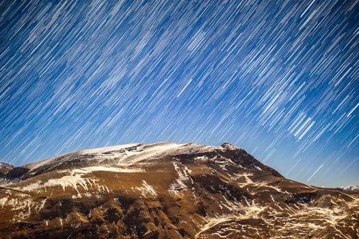 Breathtaking view of star trails streaking across a clear winter night sky over a snowy mountain landscape.