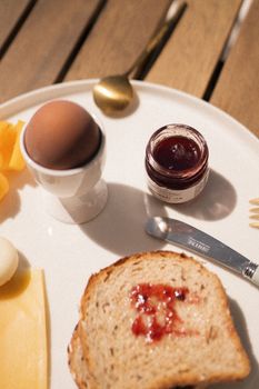 Overhead view of a rustic breakfast setup featuring bread with jam, egg, and cheese on a wooden table.