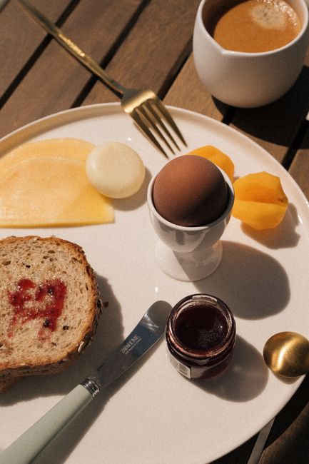 A stylish breakfast scene featuring boiled egg, toast with jam, cheese, and coffee on a wooden table.