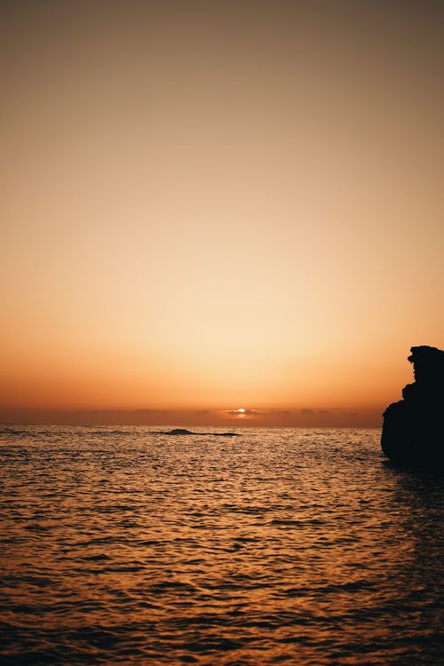 Free Tranquil sunset on a rocky seashore with vibrant orange hues reflecting on calm ocean waves. Stock Photo