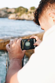 A man capturing a scenic coastal view with a digital camera outdoors.