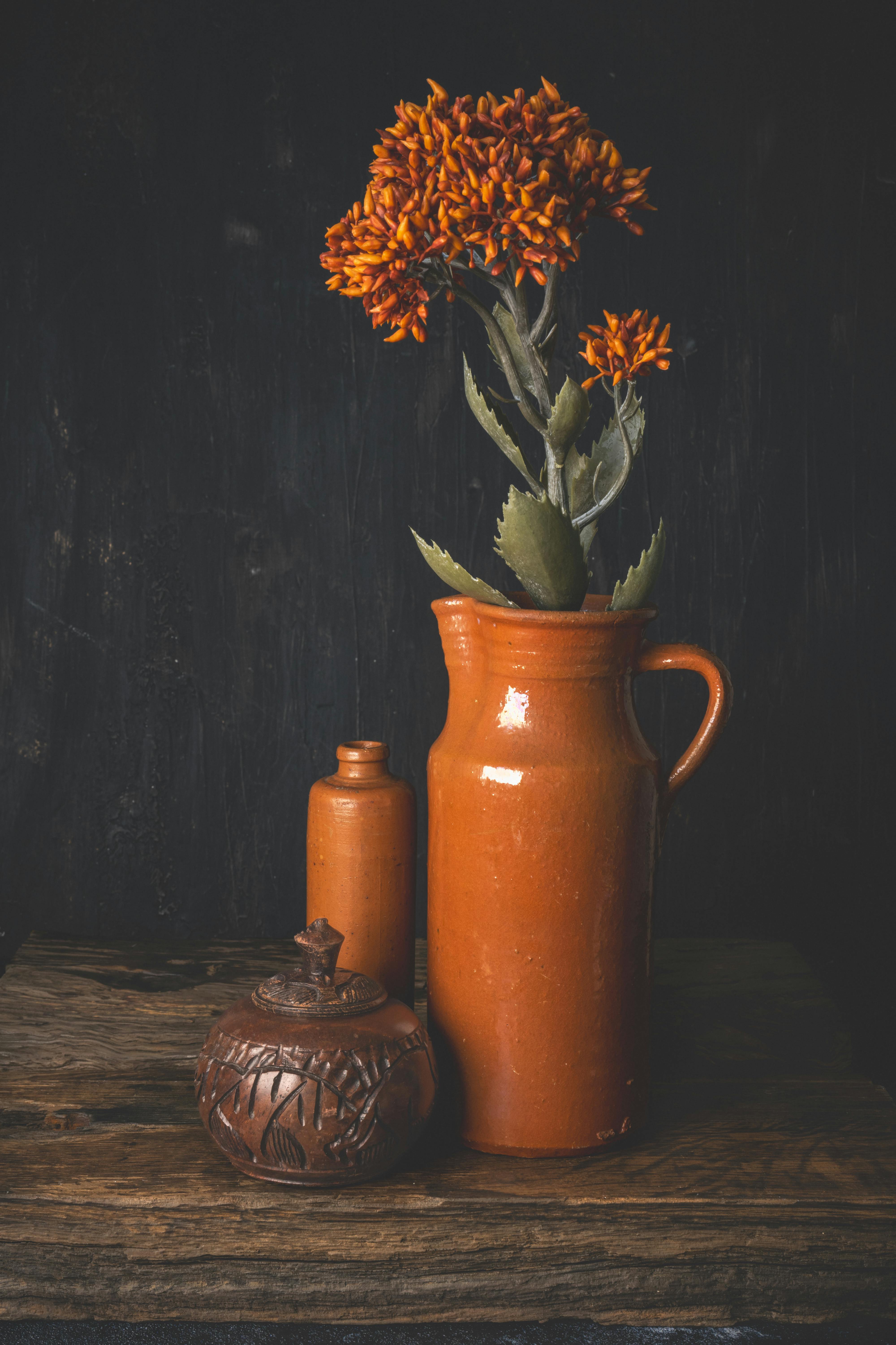 Artistic arrangement featuring orange flowers and rustic pottery on a wooden table.