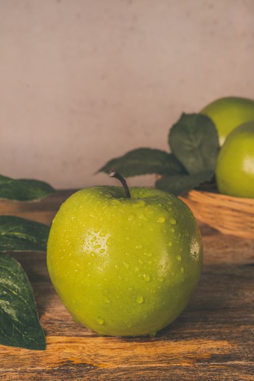 Free A close-up of a fresh green apple with water droplets, placed on a rustic wooden table. Stock Photo