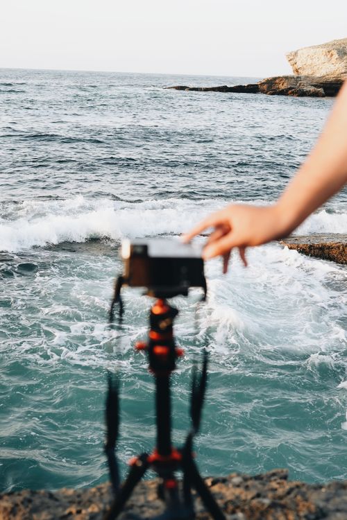 Free Photographer setting up camera on seaside cliff to capture ocean waves. Stock Photo